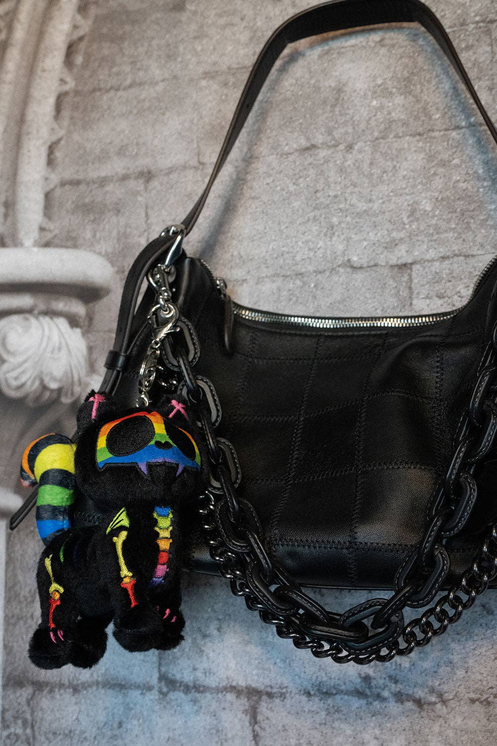 Black leather handbag with a colorful keychain attached, placed on a stone surface.