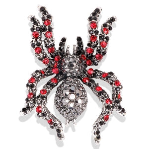Spider-shaped brooch with red and black gemstones on a white background