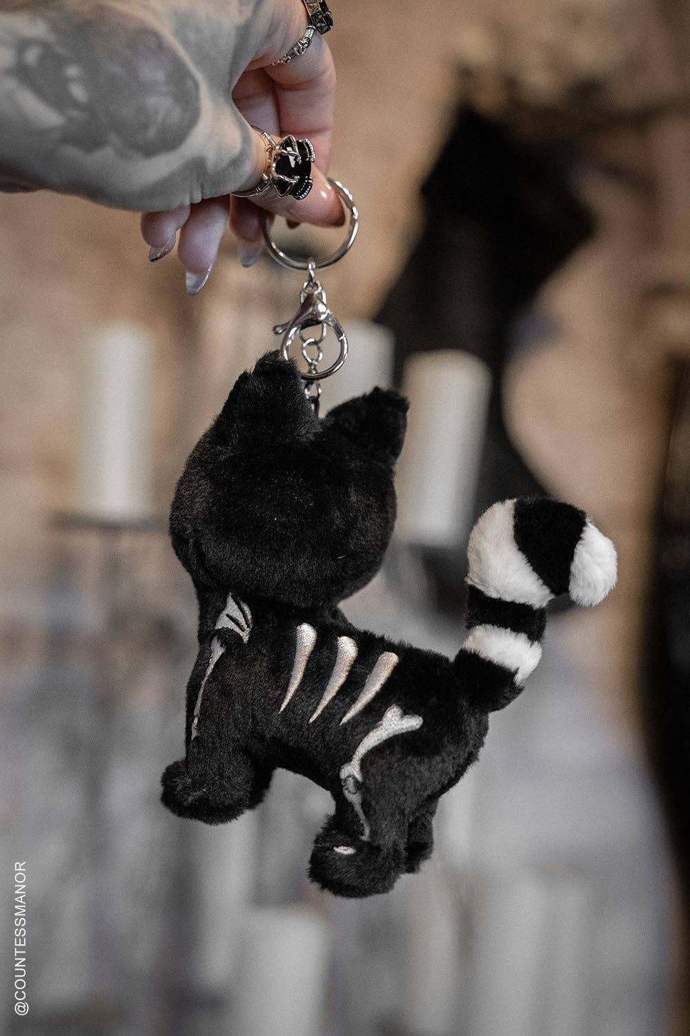 Black and white skeleton cat keychain held by a hand with tattoos.