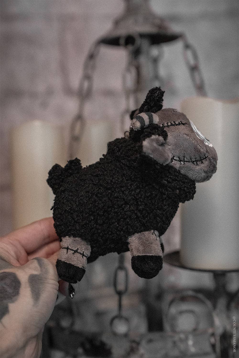 Black sheep plush toy held by a hand with a blurred background