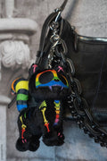 Black plush toy with rainbow accents attached to a black chain, hanging from a black leather bag.