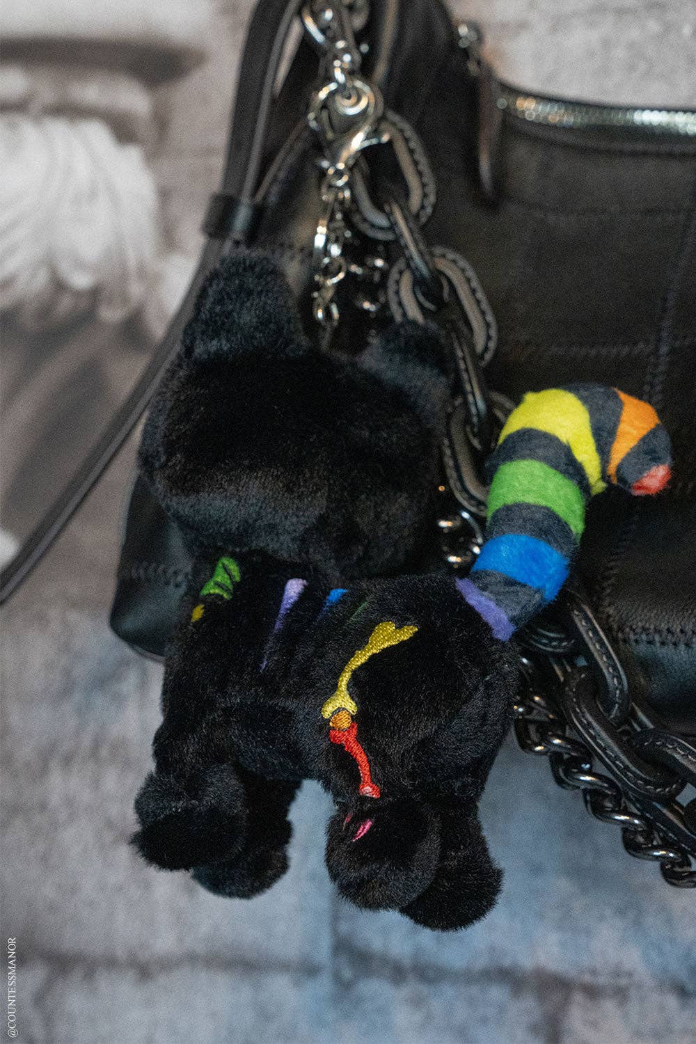 Black plush keychain with colorful accents attached to a black handbag.