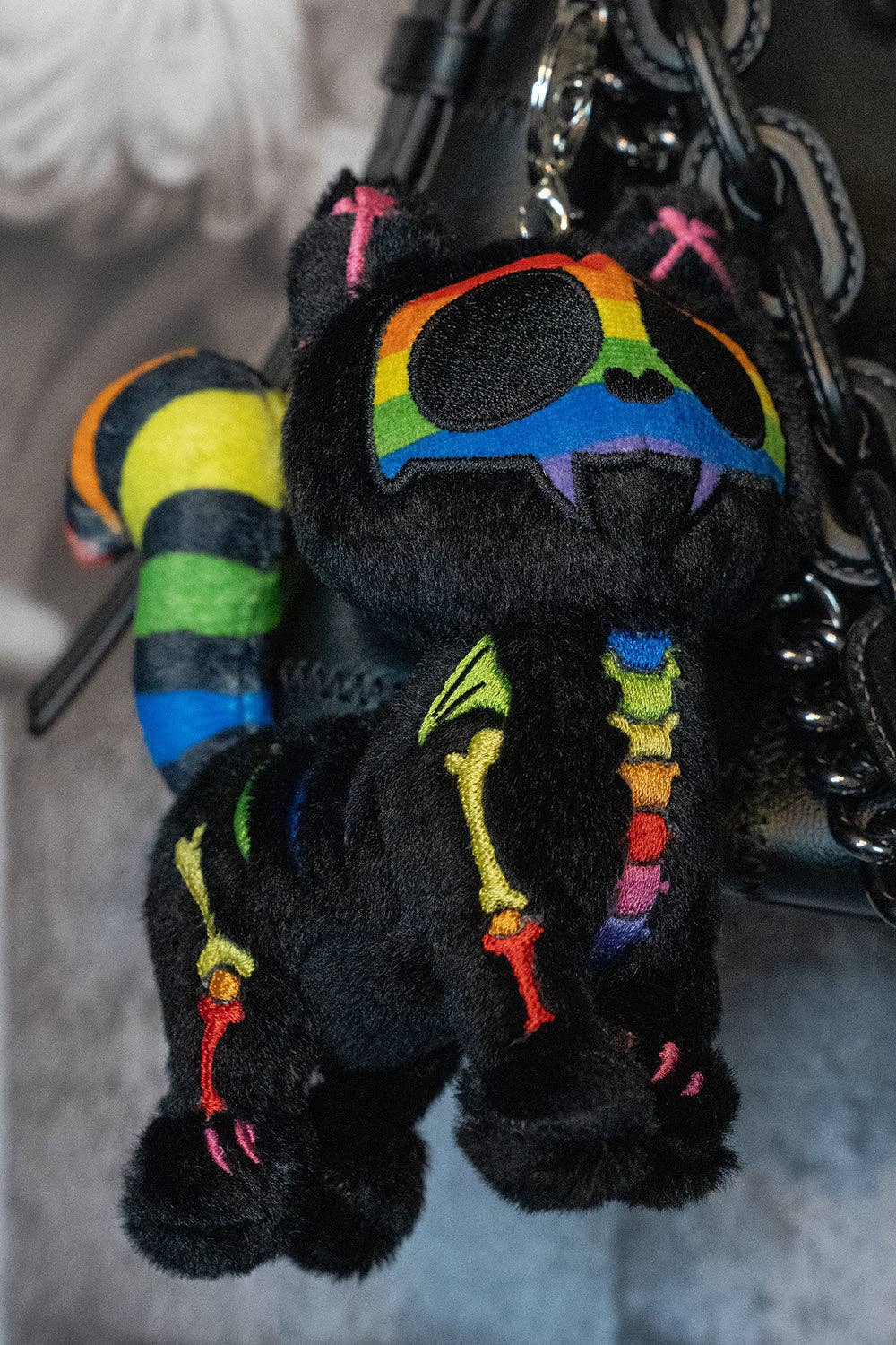 Black plush keychain with rainbow accents on a gray background