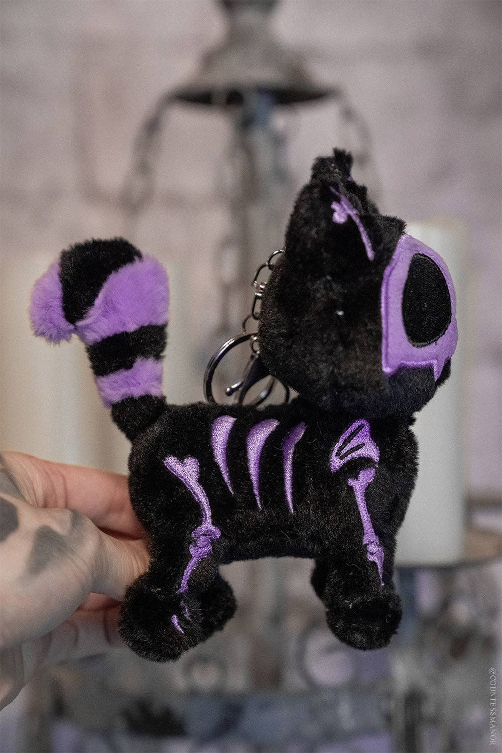 Black plush keychain with purple accents held by a hand against a blurred background
