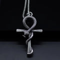A silver-toned metal pendant necklace featuring an ankh symbol with a coiled snake wrapping through it, suspended from a beaded chain against a dark background.