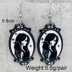 A pair of gothic-style oval dangle earrings with black and white illustrated portraits of a woman, shown against a light gray textured background. White text overlays indicate the size as 6.