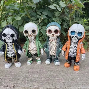 Four cartoon skeleton figurines standing side by side outdoors on a concrete surface with green foliage in the background. The skeletons wear different outfits: black hoodie, green jacket, teal jacket, and orange hoodie, with white bones and colorful shoes.