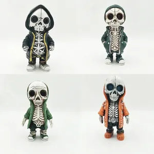 Four small skeleton-themed figurines arranged in a 2x2 grid on a plain white background. Each figure has a white skull face and torso with black skeletal details, plus different colored outer garments: black with gold trim, dark green, dark green, and orange.