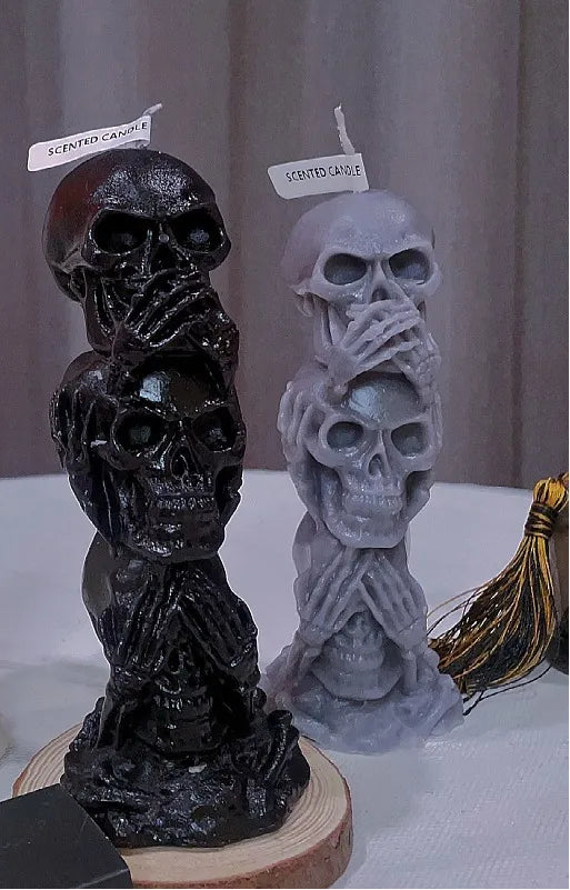 Three skull-shaped candles with labels on a white surface.