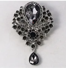 A silver-toned brooch featuring a large teardrop-shaped black gemstone surrounded by smaller black stones, with a smaller matching teardrop drop hanging below.