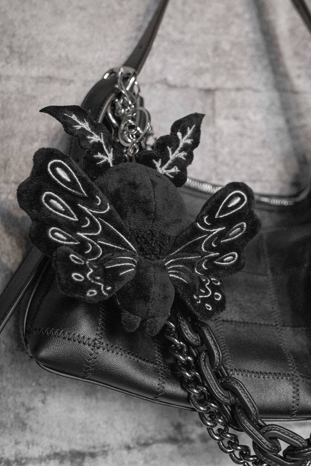Black moth man plush keychain attached to a black handbag on a textured surface