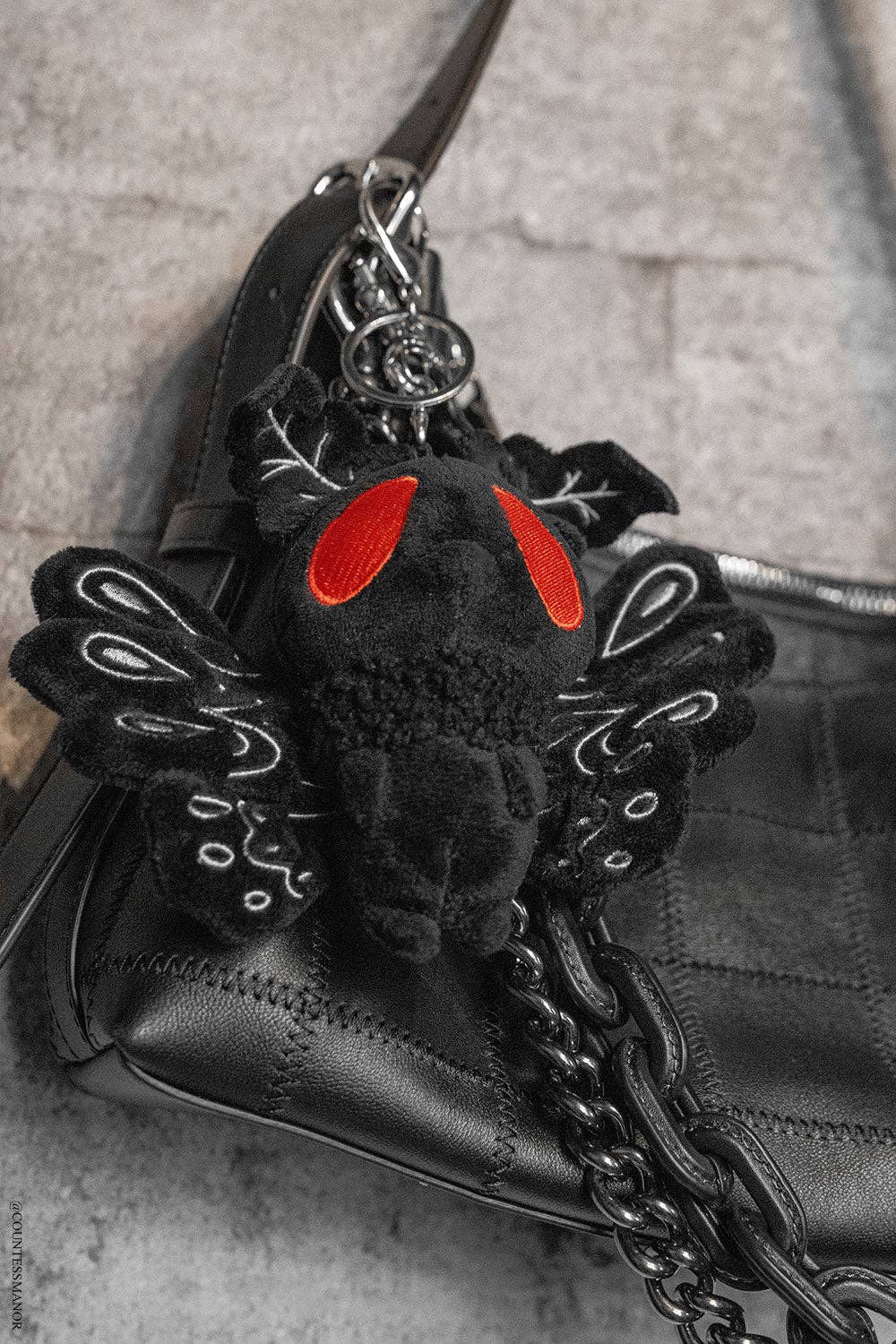 Black moth man plush keychain with red eyes on a black handbag.