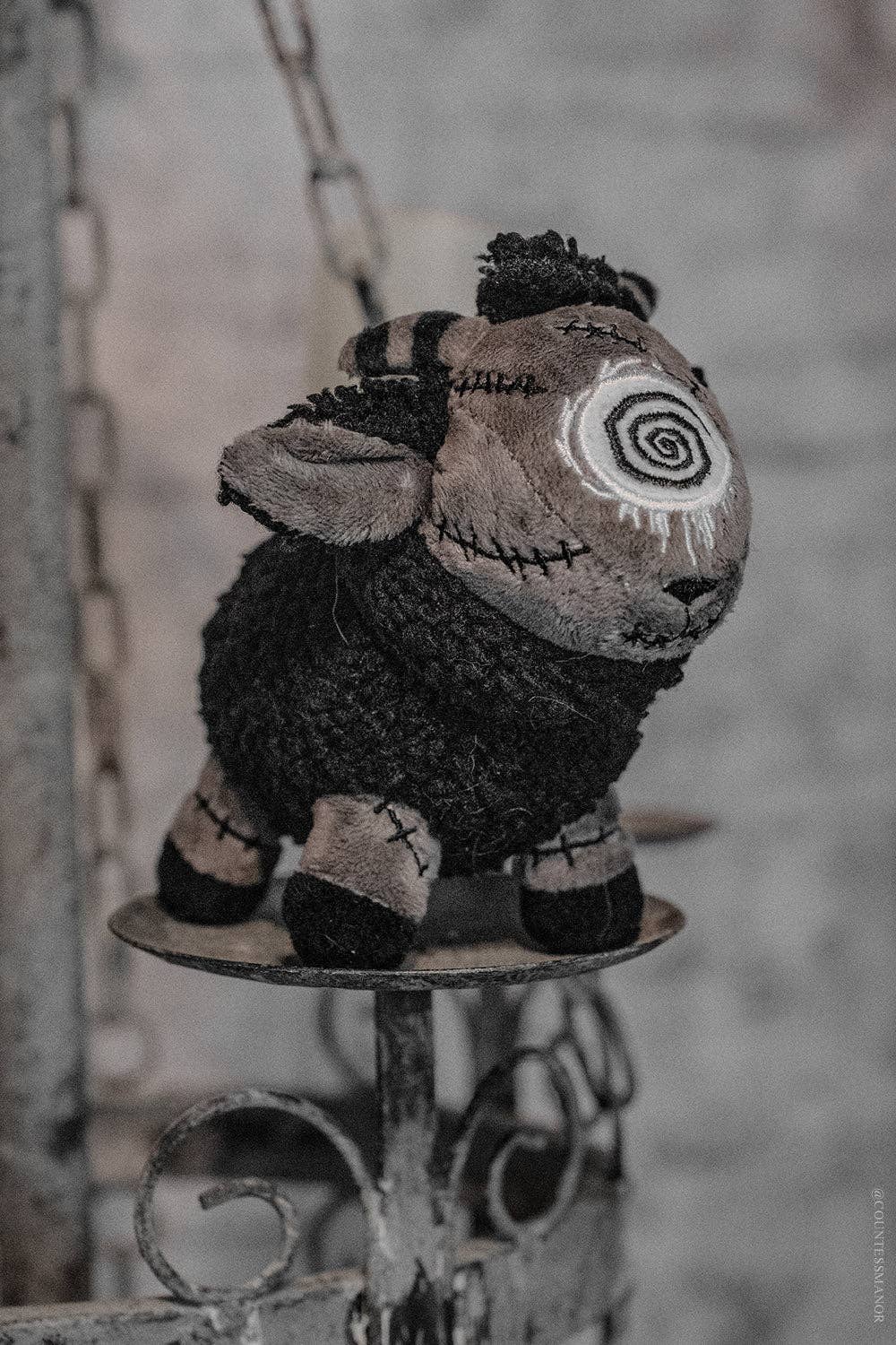 Black sheep plush keychain with spiral pattern on a stand against a blurred background