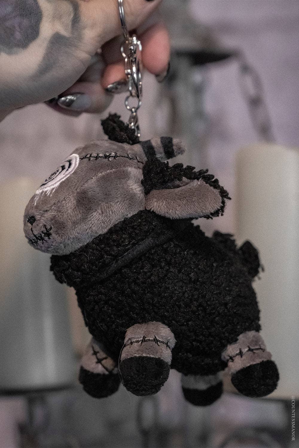 Black sheep plush keychain with black and gray color scheme held by a hand.