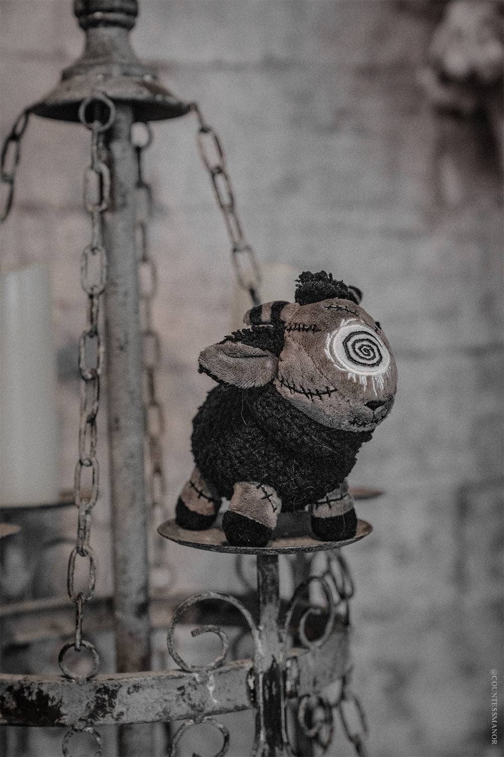 Black sheep plush toy on a metal stand with a blurred background
