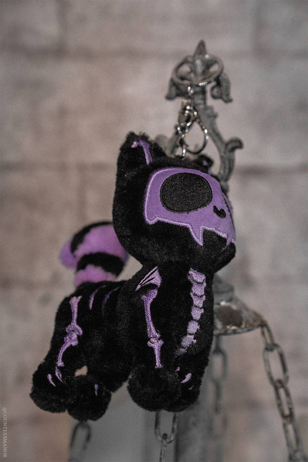 Black and purple skeleton cat plush keychain on a chain against a blurred background