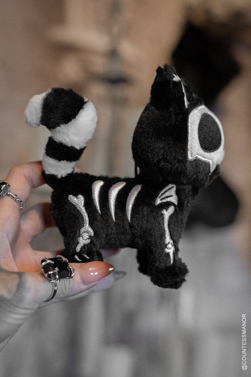 Black and white skeleton plush toy held by a hand with painted nails.